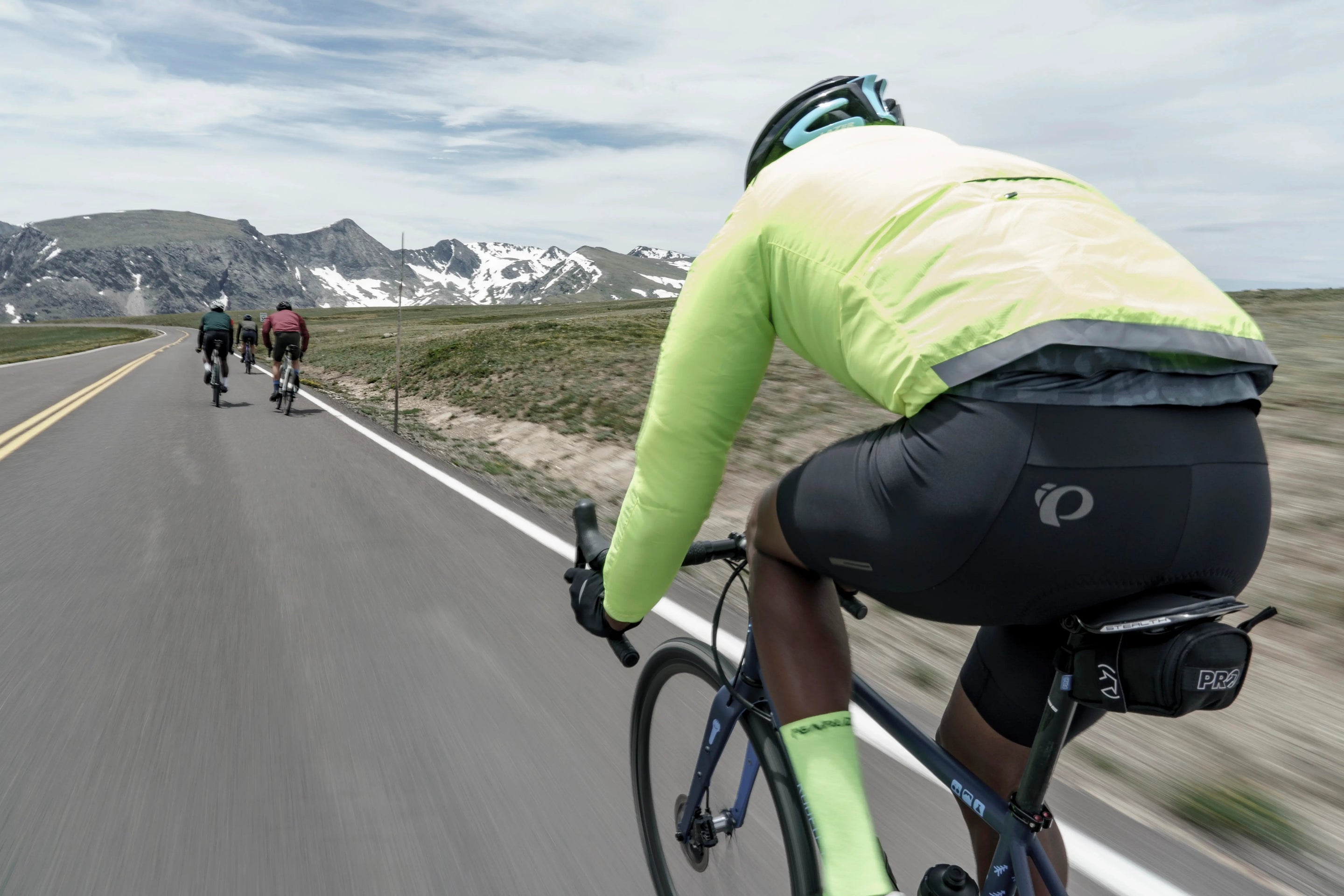 cyclist riding in Screaming Yellow BioViz PEARL iZUMi Jacket and black bibs with PEARL iZUMi reflective logo